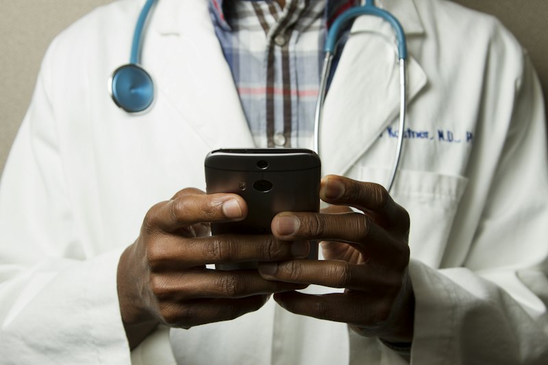 Clinician in a white coat with a stethoscope using a smartphone