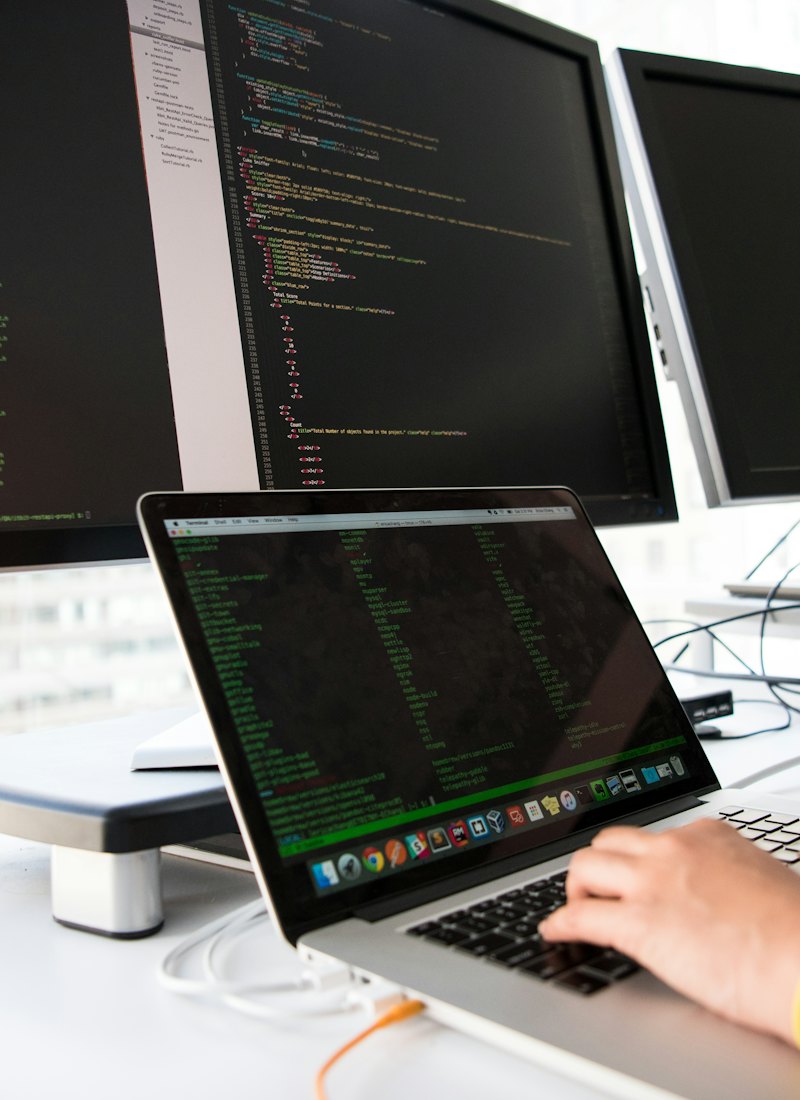 Engineer at a laptop in front of two monitors showing source code and logs