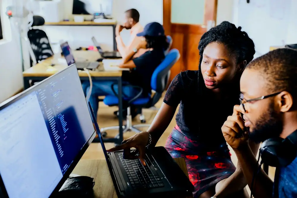 Two engineers reviewing code together on a laptop in an open-plan office