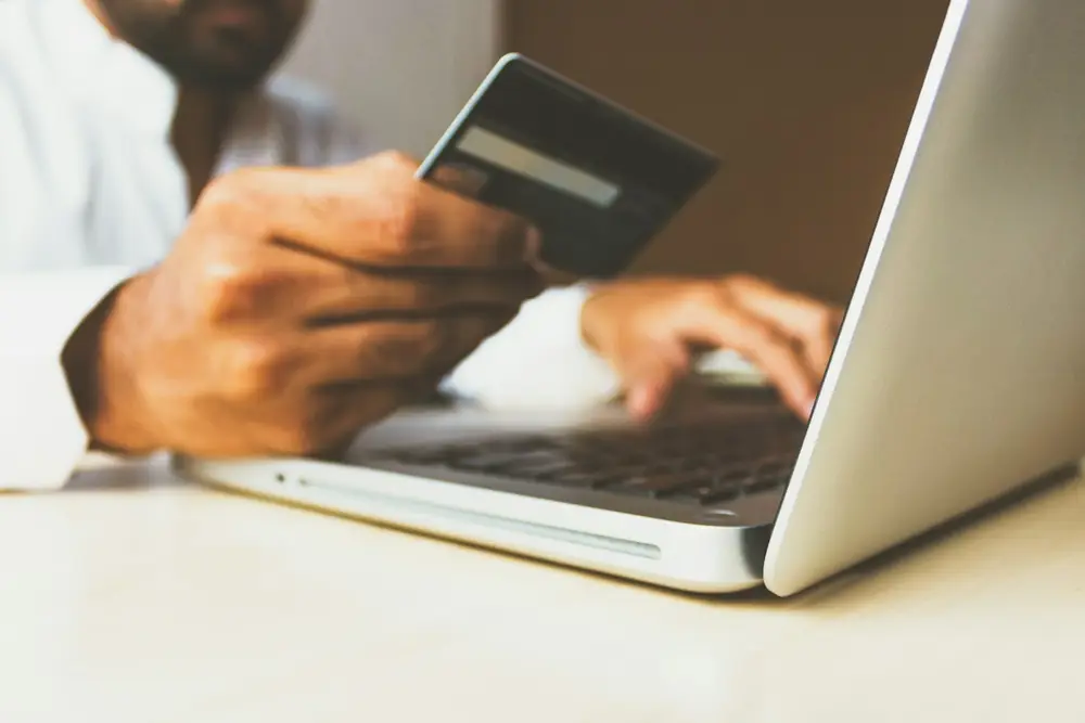 Person holding a payment card while typing on a laptop