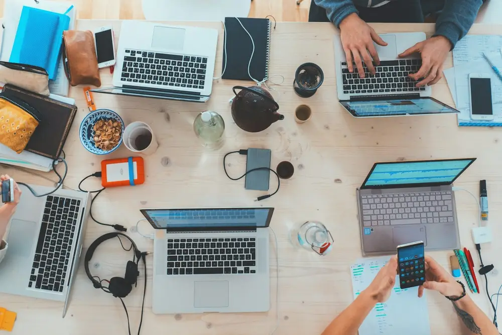 Overhead view of a team working at a shared table covered with laptops and notebooks