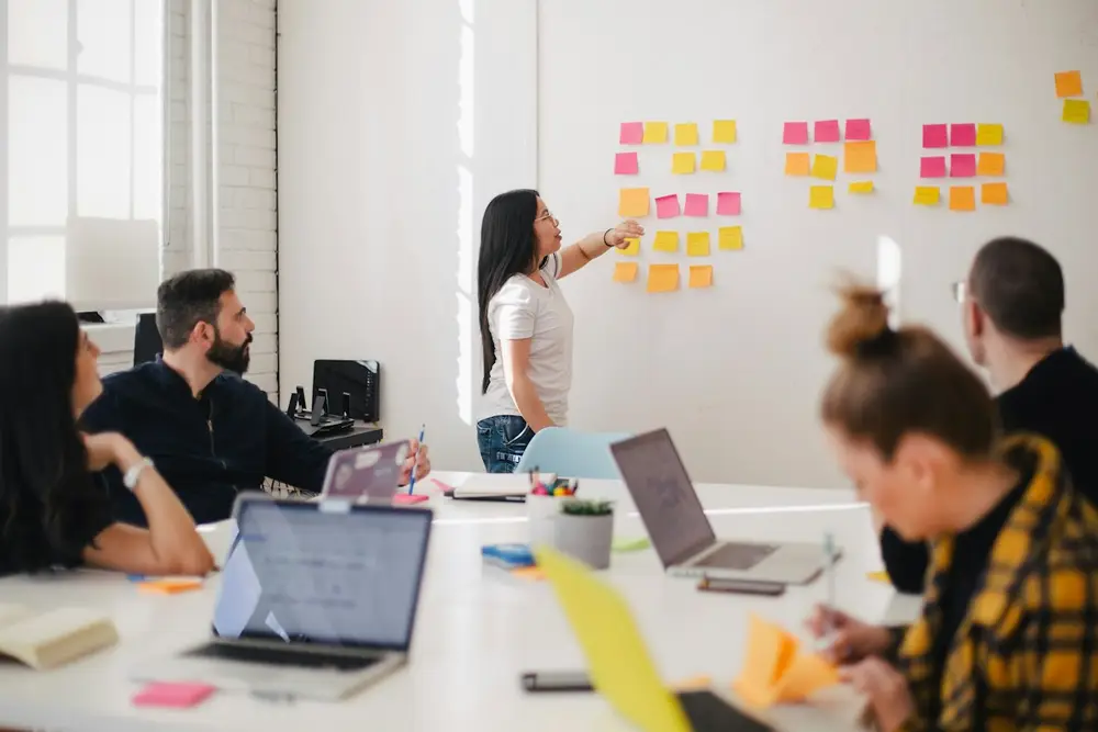 Team in a workshop while one person points at sticky notes on a whiteboard