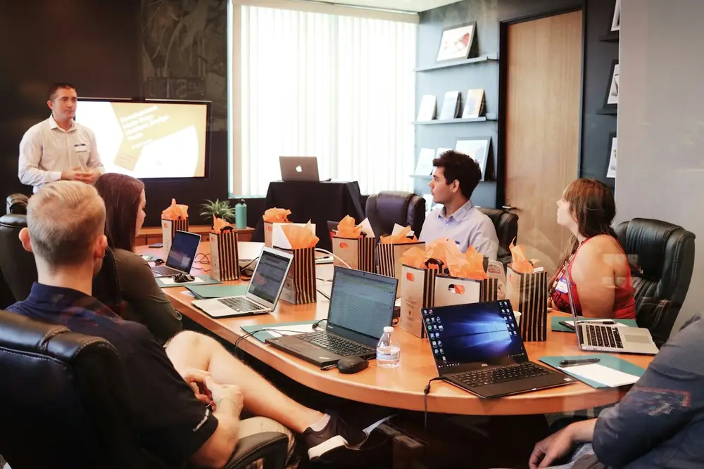 Team around a boardroom table with laptops, listening to a presentation