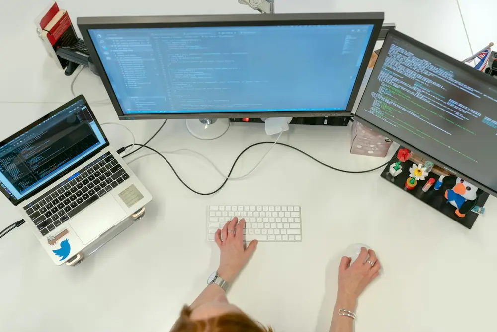 Overhead view of a developer desk with two monitors of code and a laptop