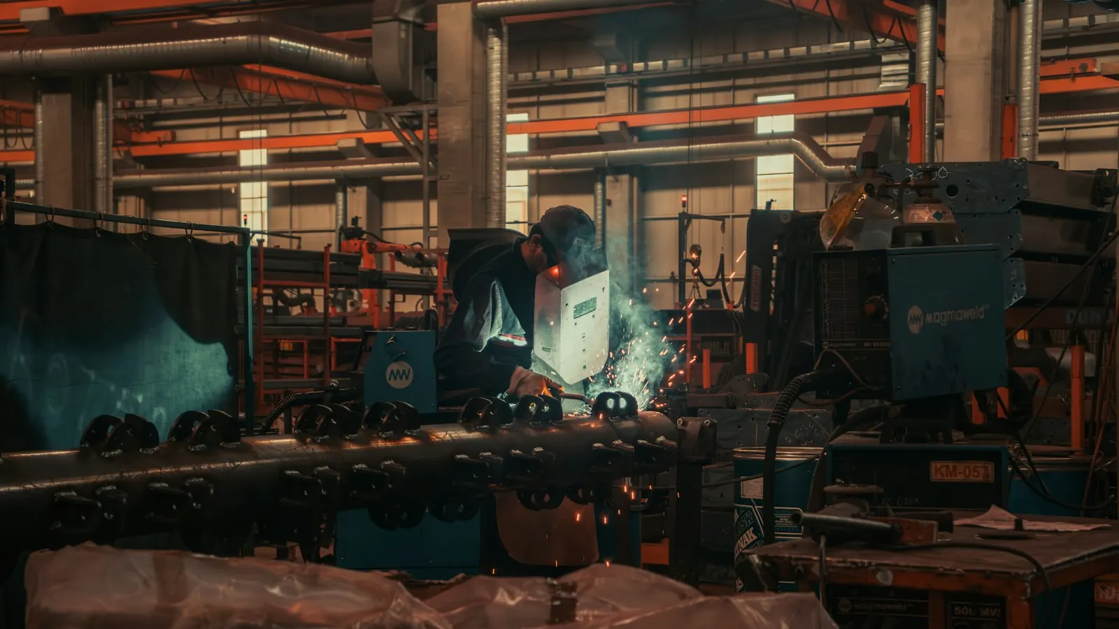 Welder at work on a busy fabrication shop floor
