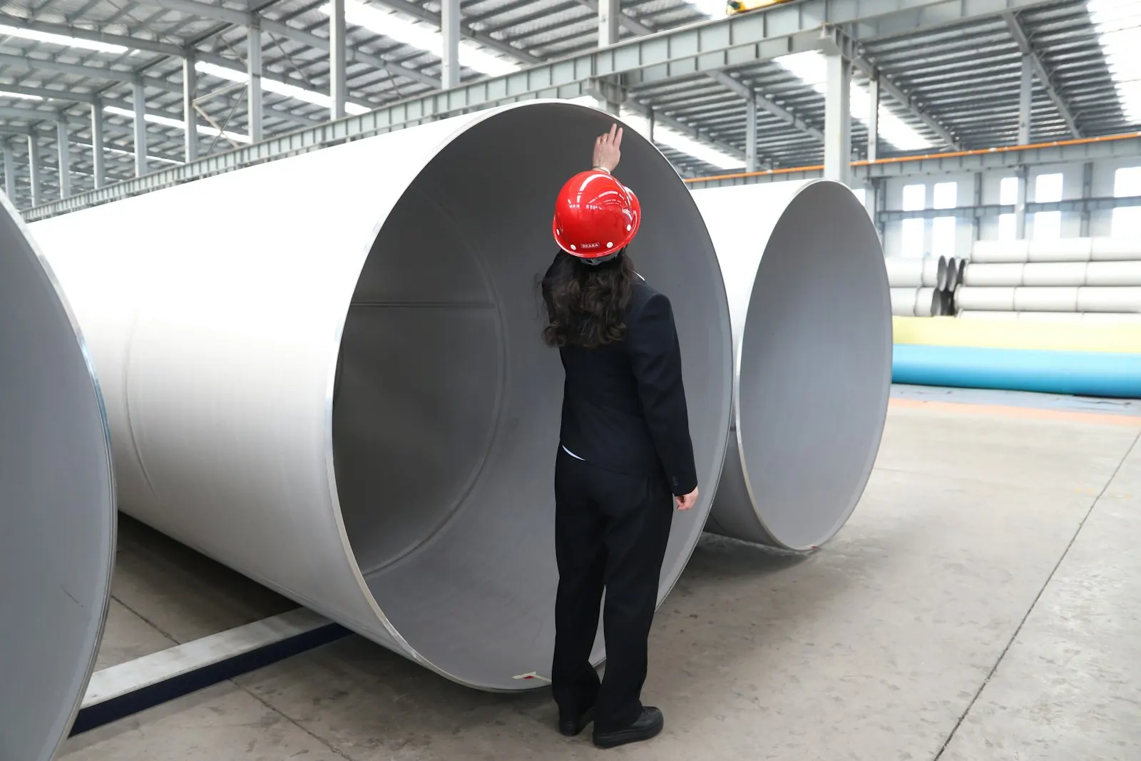 Inspector in a hard hat checking large steel pipes in a factory