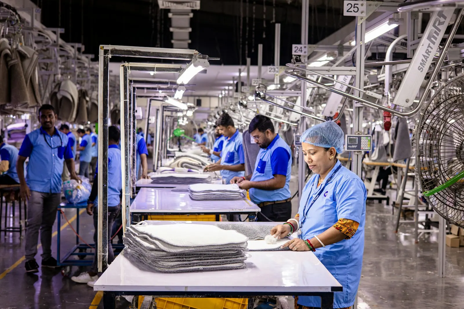 Workers in blue uniforms at stations along a busy garment production line